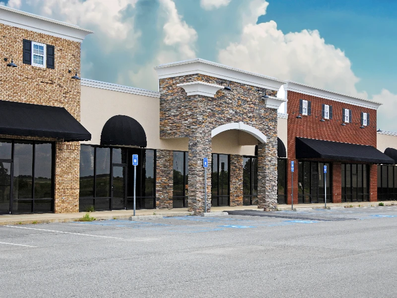 Empty storefronts in a small shopping plaza with brick and stone facades under a partly cloudy sky. commercial restoration services