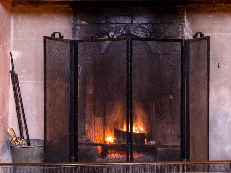 Fire burning behind a black mesh fireplace screen in a stone hearth. fire damage restoration
