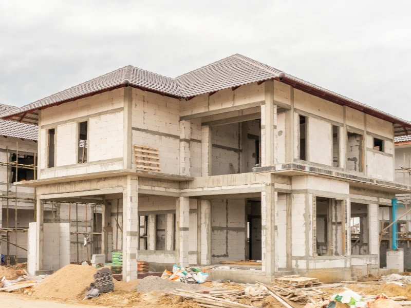 Two-story house under construction with exposed concrete blocks and a tiled roof. reconstruction services