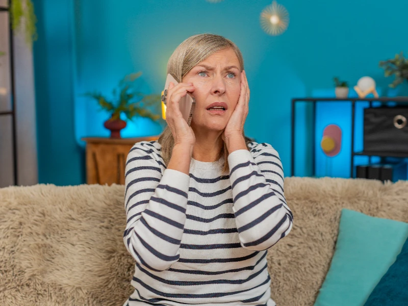 Woman with striped shirt sitting on a couch, holding a phone to her ear with a worried expression.